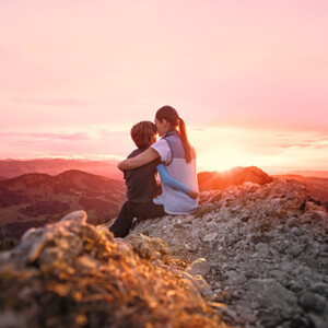 Une mère, son enfant dans les bras, est assise au sommet d'une montagne et contemple le coucher de soleil