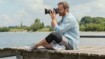 A photographer sits on a jetty with his camera and takes pictures.