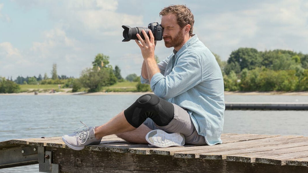 Knieschmerzen Infoseite Ein Fotograf sitzt auf einem Steg. Er trägt eine Juzo Kniebandage