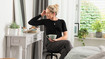 A woman with a black thorax support sits in front of a dressing table, holding a cup of tea