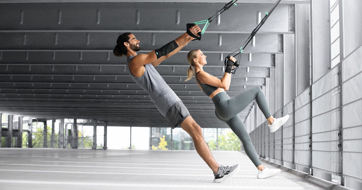 Un homme et une femme s'entraînent dans un parking souterrain avec une sangle TRX