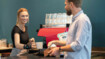 A bakery shop assistant hands a customer a coffee cup. She is wearing a wrist bandage.