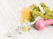Ein Glas Orangensaft, ein Apfel, Salat und ein rosa Gewicht liegen auf einem Tisch und sind mit einem Maßband umwickelt
