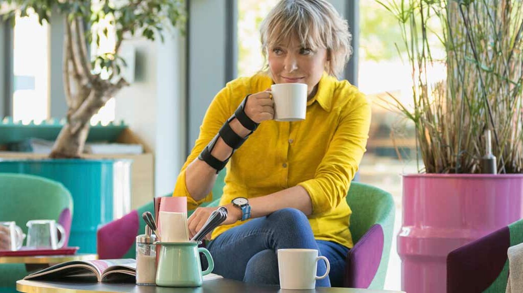 En kvinde sidder på en café og har en håndledsortose på sin højre hånd. En kvinde sidder på en café og har en håndledsortose på sin højre hånd.