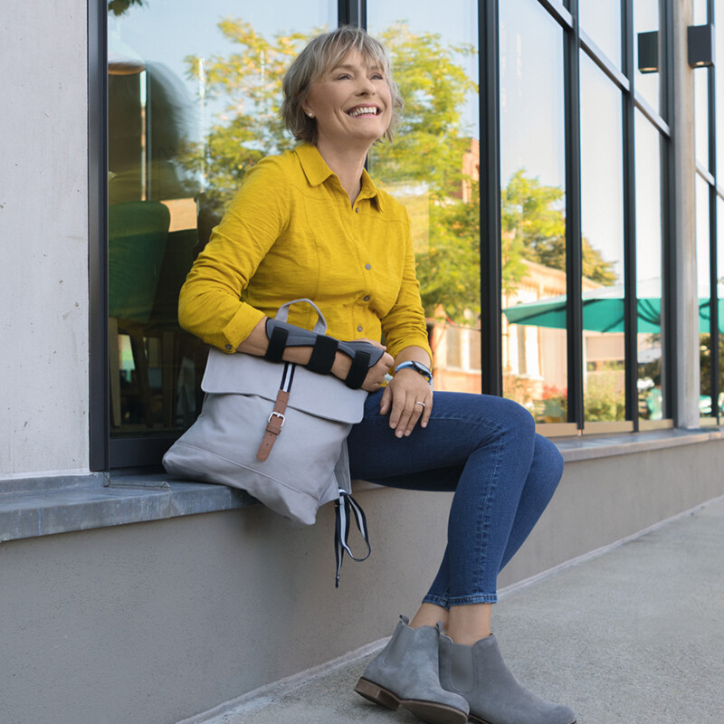 A woman is sitting on a windowsill, holding her bag. She is wearing a wrist brace A woman is sitting on a windowsill, holding her bag. She is wearing a wrist brace