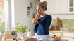 Woman with a dark-blue thorax support sitting on a kitchen counter, drinking orange juice