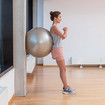 A woman leaning upright against a wall with an exercise ball