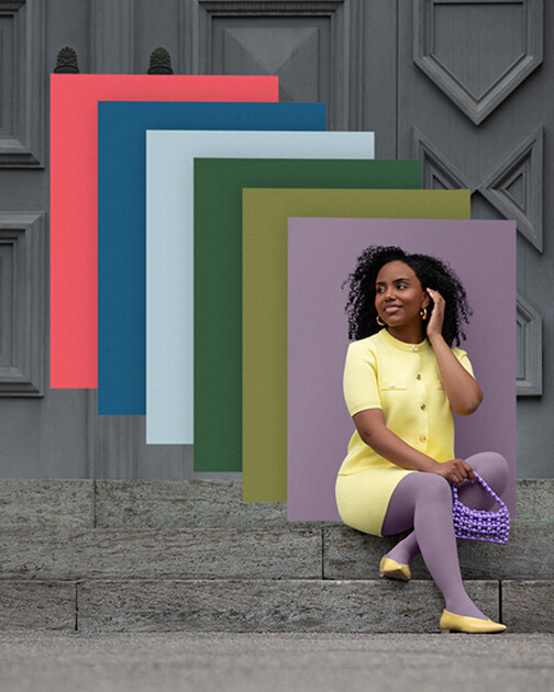Una mujer con medias de compresión en color Cozy Violet está sentada en unas escaleras. Al fondo, los paneles de color de la actual colección Juzo Trend Colours. Una mujer con medias de compresión en color Cozy Violet está sentada en unas escaleras. Al fondo, los paneles de color de la actual colección Juzo Trend Colours.