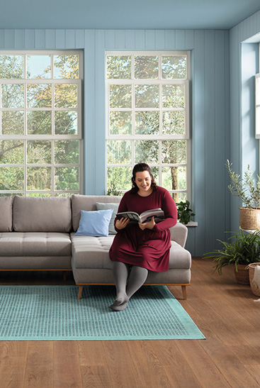 Woman standing in front of her couch, smiling and holding some papers