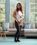 Lifestyle Image Juzo Sensation Fit Woman standing in front of her couch, smiling and holding some papers